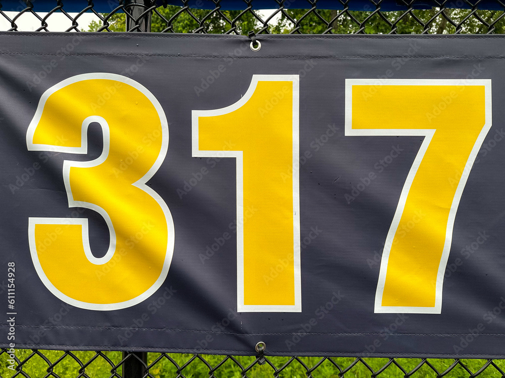317 foot ft baseball field distance sign in yellow and black mounted on the black vinyl outfield fence.
