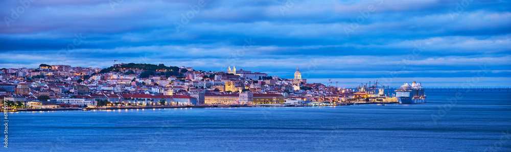 Obraz premium View of Lisbon over Tagus river with passing ferry boat from Almada with moored cruise liner in evening twilight. Lisbon, Portugal
