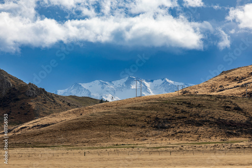 Photograph of transmission lines running over a hill against a blue sky and snow capped mountains on the South Island of New Zealand