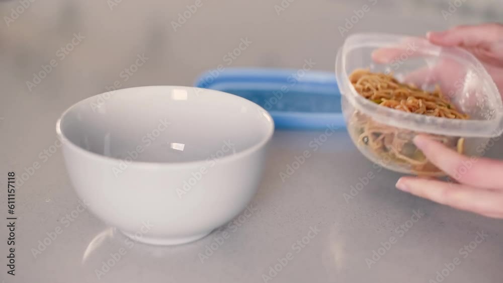 Abriendo un tupperware y vertiendo fideos en un bol sobre la encimera de una cocina. Concepto de conservar comida preparada en un envase de plástico.
