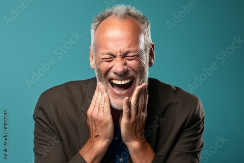 Headshot portrait photography of a grinning mature man placing the hand over the mouth in a laughter gesture against a sea-green background. With generative AI technology