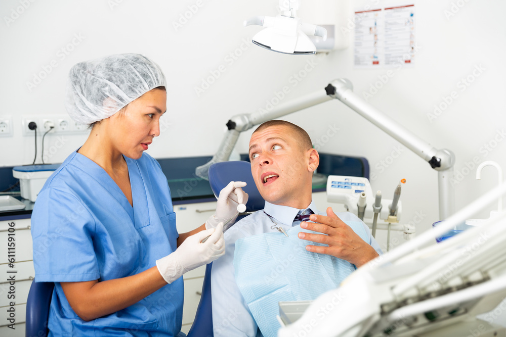 Obraz premium Qualified woman dentist working in the clinic examines a man patient sitting in a dental chair