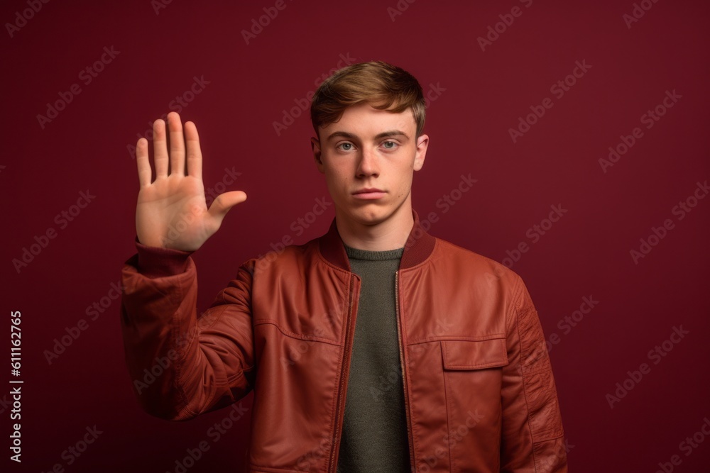 Medium shot portrait photography of a satisfied boy in his 20s making a no or stop gesture with the extended palm against a rich maroon background. With generative AI technology
