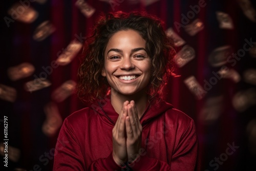 Headshot portrait photography of a joyful girl in her 20s making a money gesture rubbing the fingers against a rich maroon background. With generative AI technology