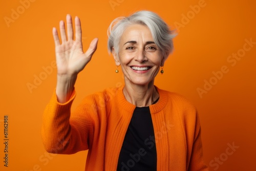 Close-up portrait photography of a satisfied mature woman waving with the hand against a tangerine orange background. With generative AI technology