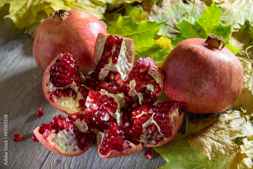 Two fresh ripe pomegranates and one cut on a gray wooden table and yellow autumn leaves. Close-up