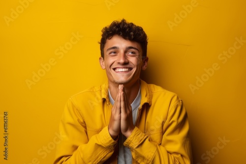 Medium shot portrait photography of a happy boy in his 20s putting hands together as if praying against a yellow background. With generative AI technology