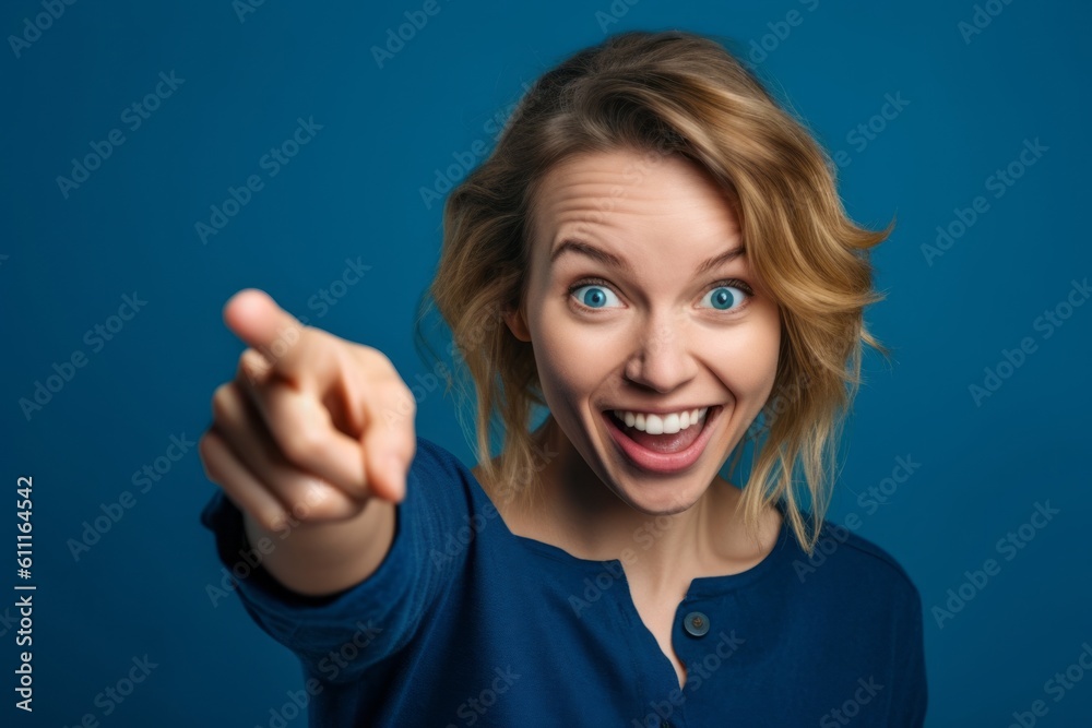 Close-up portrait photography of a happy girl in her 30s pointing up against a sapphire blue background. With generative AI technology