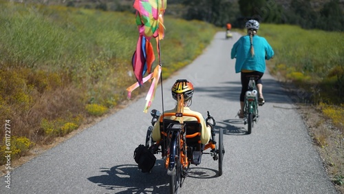 Rear view of mother and daughter biking together riding recumbent and normal electric e bikes.