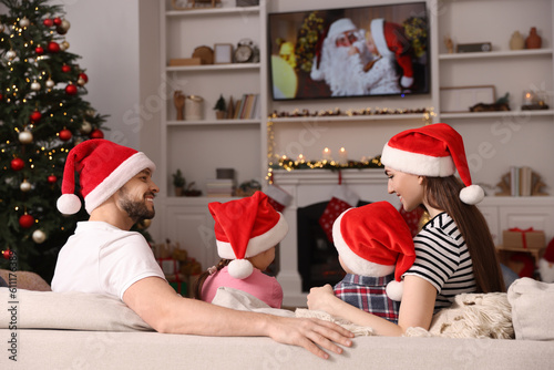 Happy family wearing Christmas hats spending time near TV in cosy room. Winter holidays atmosphere