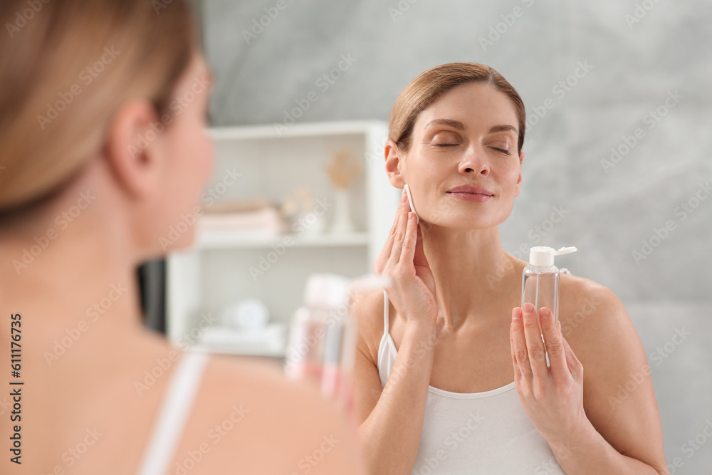 Beautiful woman removing makeup with cotton pad near mirror indoors Beautiful woman removing makeup with cotton pad near mirror indoors