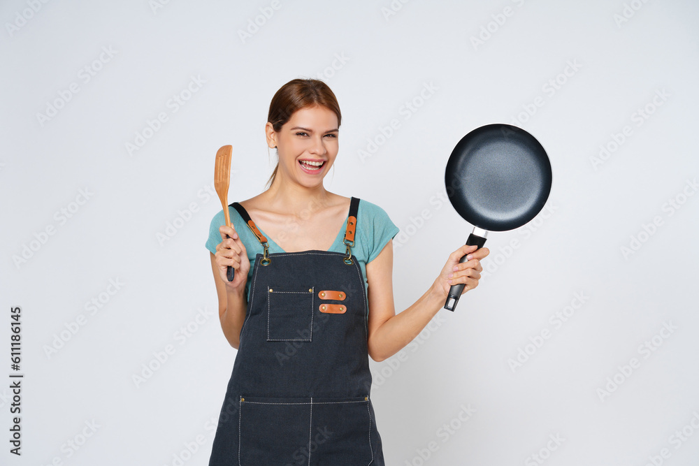 Young woman wearing kitchen apron cooking and holding pan and spatula isolated on white background. Young woman wearing kitchen apron cooking and holding pan and spatula isolated on white background.
