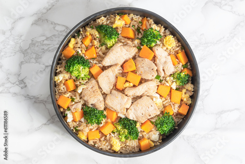 Fried rice with chicken breast has vegetable broccoli pumpkin in bowl on white marble table.