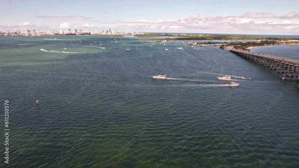 Tracking aerial drone shot above the water in Miami Florida. Drone tracking yachts which moving from under the bridge. William M Powell Bridge and beautiful cityline reveals in the shot. Tracking aerial drone shot above the water in Miami Florida. Drone tracking yachts which moving from under the bridge. William M Powell Bridge and beautiful cityline reveals in the shot.