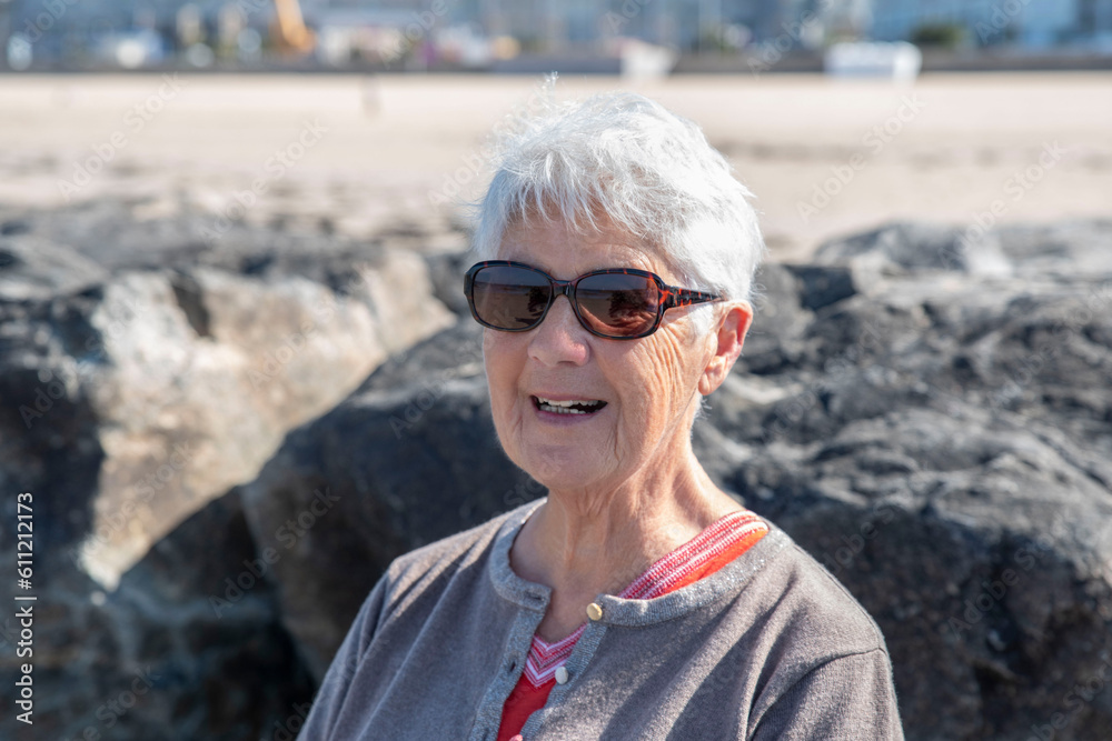 A senior woman on a beach in summer with white hair and sunglasses A senior woman on a beach in summer with white hair and sunglasses