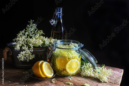 Homemade elderflower syrup in jar and elderberry flowers on wooden table - dark and moody photography