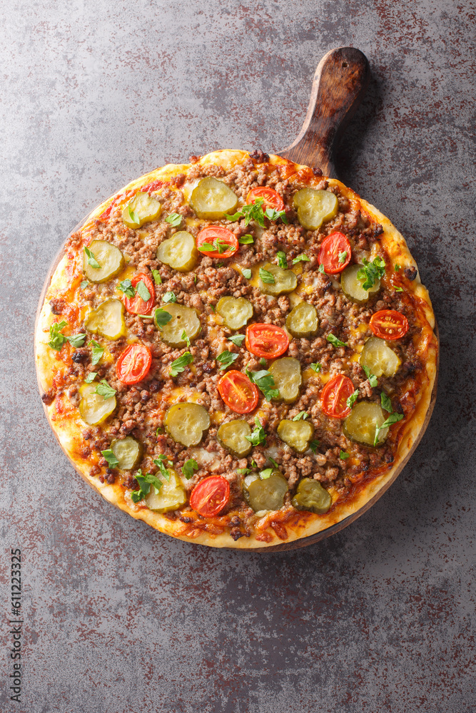 Hot pizza with ground beef, tomatoes, pickled cucumbers and cheese close-up on a wooden board on the table. Vertical top view from above