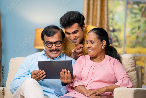 Canvas Print Indian senior parents with adult son watching digital tablet by talking together at home - concept of communication, parenthood and interaction