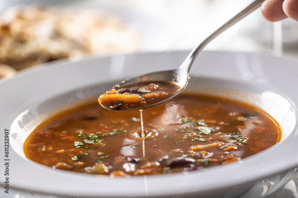 Detail of a spoon of minestrone soup above the full plate Detail of a spoon of minestrone soup above the full plate