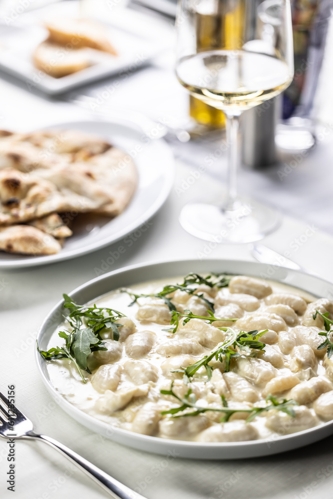 Gnocchi with white cheesy sauce topped with rocket leaves served with white wine Gnocchi with white cheesy sauce topped with rocket leaves served with white wine