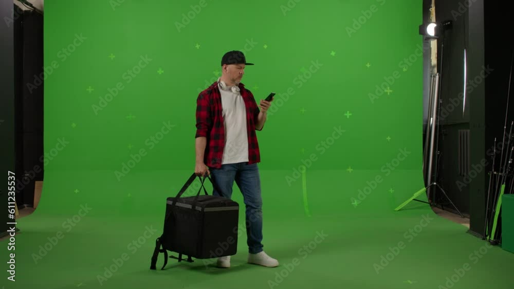 Young food courier with thermal backpack standing and looking around searching for direction on a Green Screen, Chroma Key