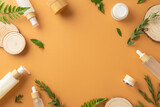 Organic cosmetic products concept. Top view photo of empty frame of cosmetic jars, bottles and tubes, fern and eucalyptus leaves and wooden podiums on isolated brown background with copyspace
