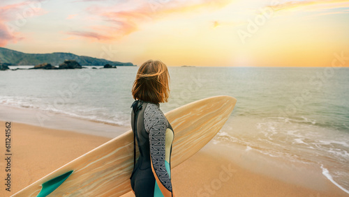 Quadro su tela Unrecognizable young surfer woman with wetsuit carrying surfboard looking to the