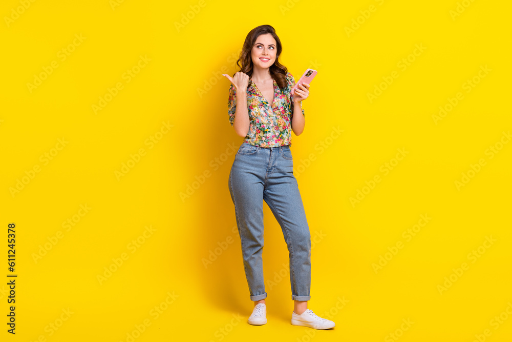 Full length photo of dreamy sweet lady wear retro flower print blouse texting device thumb empty space isolated yellow color background Full length photo of dreamy sweet lady wear retro flower print blouse texting device thumb empty space isolated yellow color background