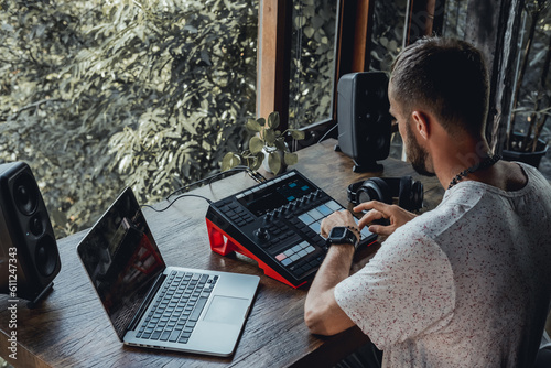 young handsome man with a beard and dark hair sits at a table and creates music, listens to headphones, writes songs, musician portrait, concept, laptop, monitor speakers, pianist, recording studio
