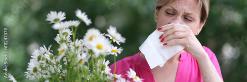 Young woman with hay fever blowing her nose in napkin near chamomile flowers. Allergic diseases concept