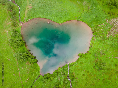 Mountain lake in shape heart with turquoise water and green shore. Aerial top down shot