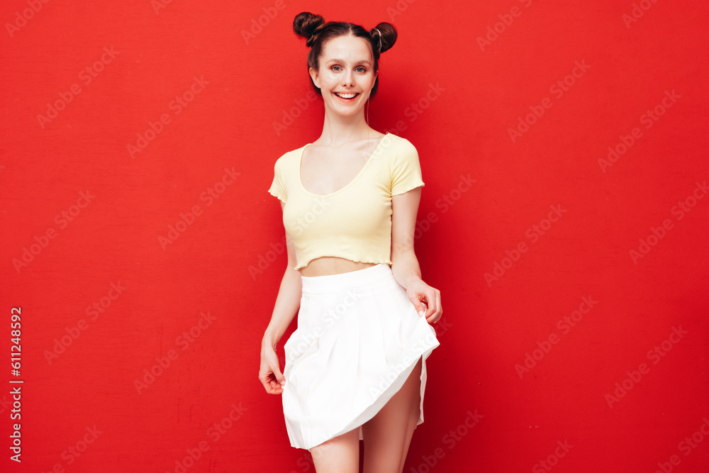 Young beautiful smiling female in trendy summer yellow t-shirt and skirt. Carefree woman with two horns hairstyle posing near red wall in studio. Positive model having fun. Cheerful and happy Young beautiful smiling female in trendy summer yellow t-shirt and skirt. Carefree woman with two horns hairstyle posing near red wall in studio. Positive model having fun. Cheerful and happy