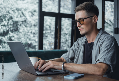 Handsome man call in smartphone, happy face, outdoor hipster portrait on the cafe, smile happy face, listen music on headphones, text, messenger, hipster, player,photo concept, laptop, coffee cup