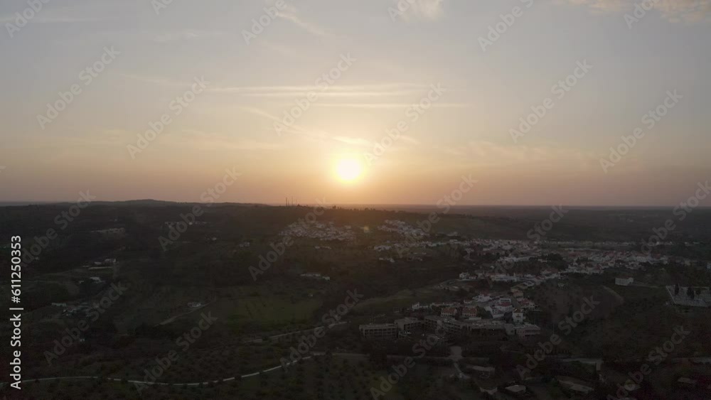 aerial view of a golden sunset in a rural field. The evening sun casts a golden glow in the cloudy sky near a small village.