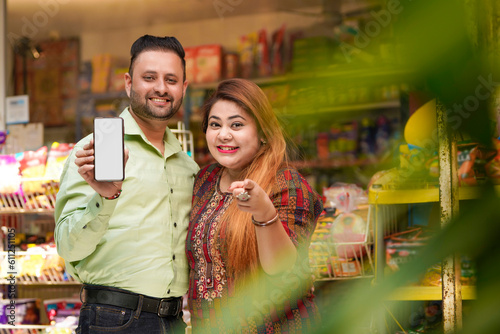 Indian couple showing smartphone screen at grocery shop.