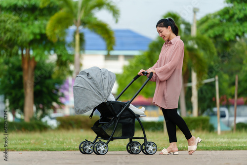 Fotografía happy mother looking and pushing infant baby stroller while walking in park