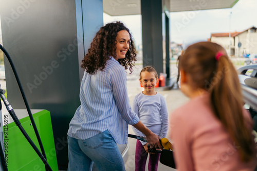 the mother fills the car with fuel at the gas station and talks to her daughters about the upcoming trip