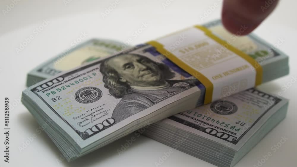 stack of bank bundles with US dollars on a white background. Close-up shot of new, freshly printed hundred-dollar bills rotating on a table. cash flow, business investment, or big money concepts. stack of bank bundles with US dollars on a white background. Close-up shot of new, freshly printed hundred-dollar bills rotating on a table. cash flow, business investment, or big money concepts.