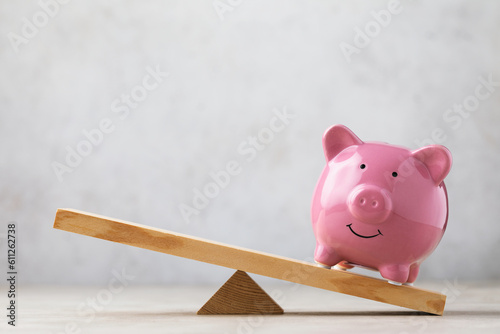Cuadro en lienzo Ceramic piggy bank on wooden swing or scales on abstract background, business co