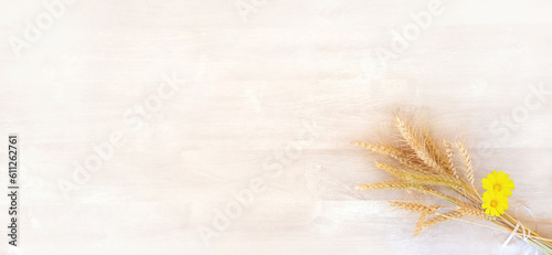 A bouquet of ripe yellow wheat with yellow flowers, on a background of a white wooden surface, is intended for a greeting card for the holiday of Shavuot, with free space for text