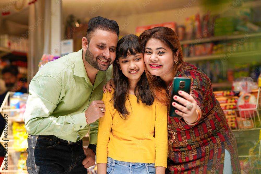 Obraz premium Indian family taking selfie in smartphone at grocery shop.
