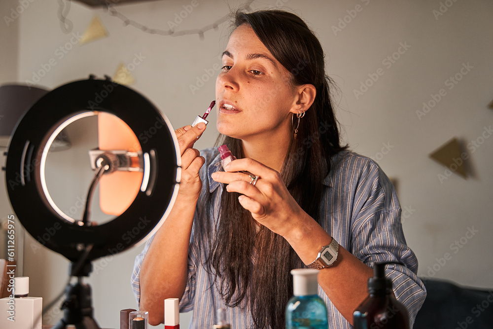 Fototapeta premium Attentive lady with long brunette hair making daily natural makeup and looking at smartphone camera