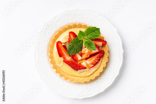 Overhead shot of strawberry mini cake tartlet with vanilla custard and mint leaves over white background. Concept of homemade sweet pastries. Copy space, top view