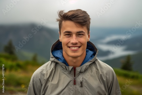 Headshot portrait photography of a grinning boy in his 30s wearing a lightweight windbreaker against a scenic mountain overlook background. With generative AI technology