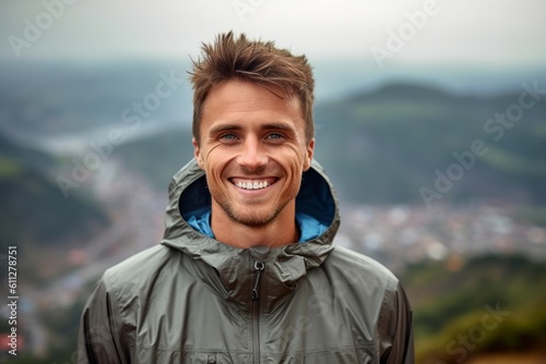 Headshot portrait photography of a grinning boy in his 30s wearing a lightweight windbreaker against a scenic mountain overlook background. With generative AI technology