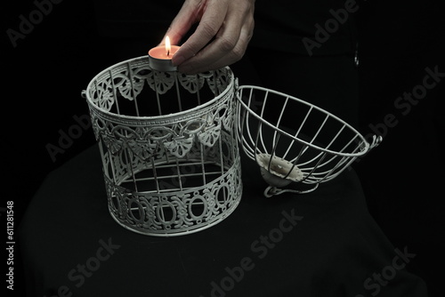 The woman has a cage in her hands. There is a candle in the cage. photo