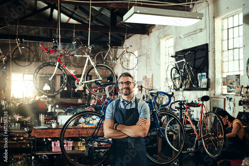 Happy, portrait and repair man in bicycle shop with arms crossed in small business workshop. Owner, bike mechanic and smile of confident person, professional or mature technician and glasses in store photo
