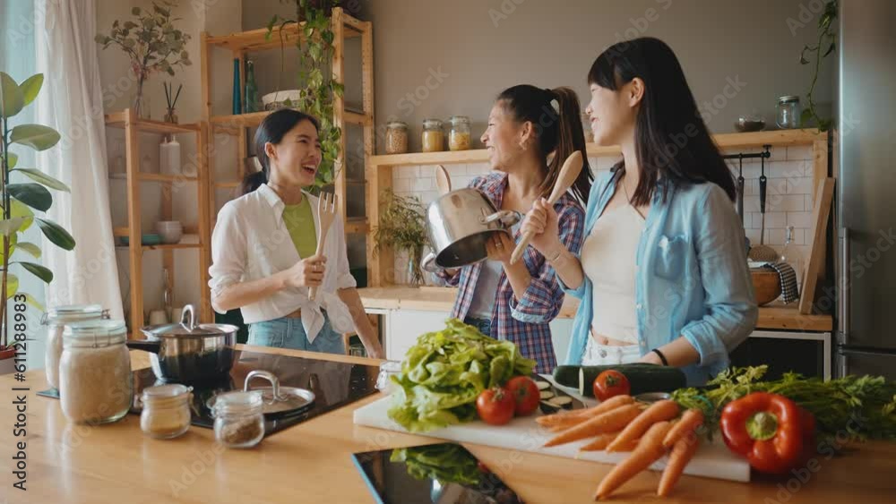 Three happy young women preparing asian food in the kitchen. Group of female friends enjoying their girls day at home cooking an healthy meal with vegetables and organic ingredients. lifestyle concept