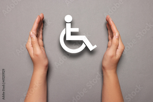 Disability inclusion. Woman protecting wheelchair symbol on grey background, closeup photo