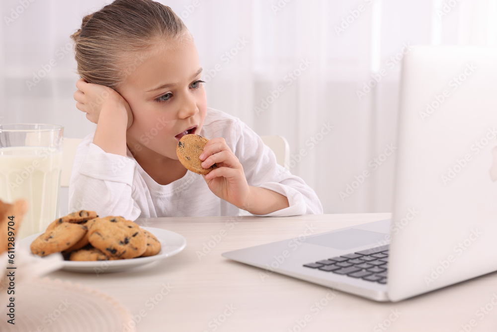 Little girl using laptop while having breakfast at table indoors. Internet addiction Little girl using laptop while having breakfast at table indoors. Internet addiction